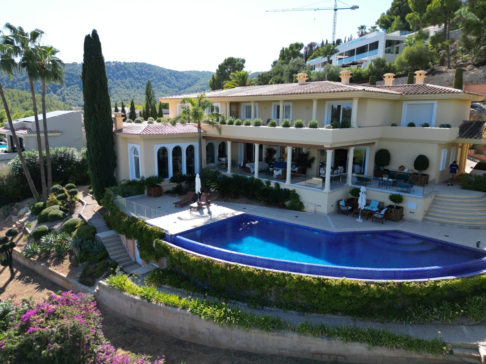 Mediterrane Villa mit geschwungenem Pool und üppiger Berglandschaft im Hintergrund.