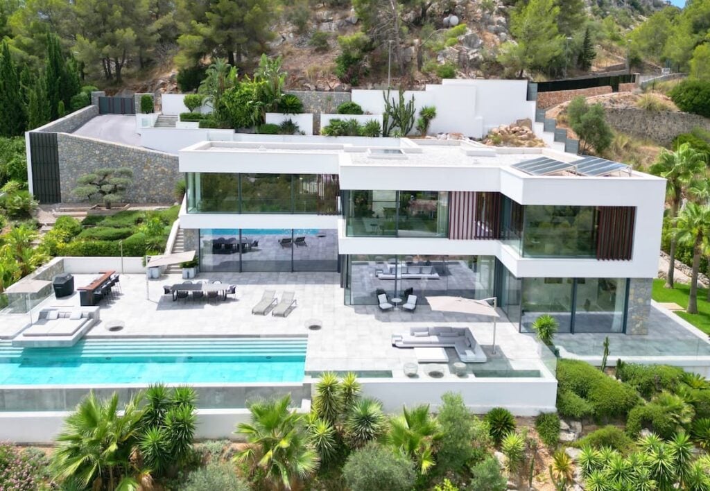 Moderne kubische Villa mit großflächigen Glasfronten, weitläufiger Terrasse und langem Infinity-Pool in Hanglage.