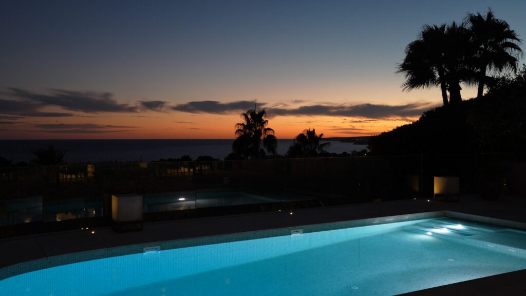 Swimming pool at dusk with indirect lighting and sea view.