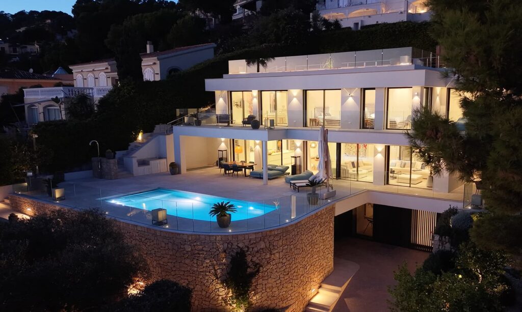 Illuminated luxury villa at night with pool and expansive front windows.