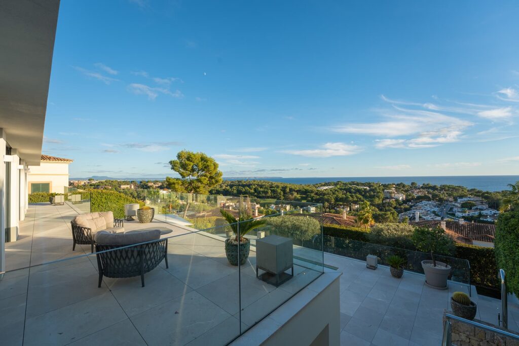 Terrace with seating area and glass balustrade with wide views over coastal town and sea.