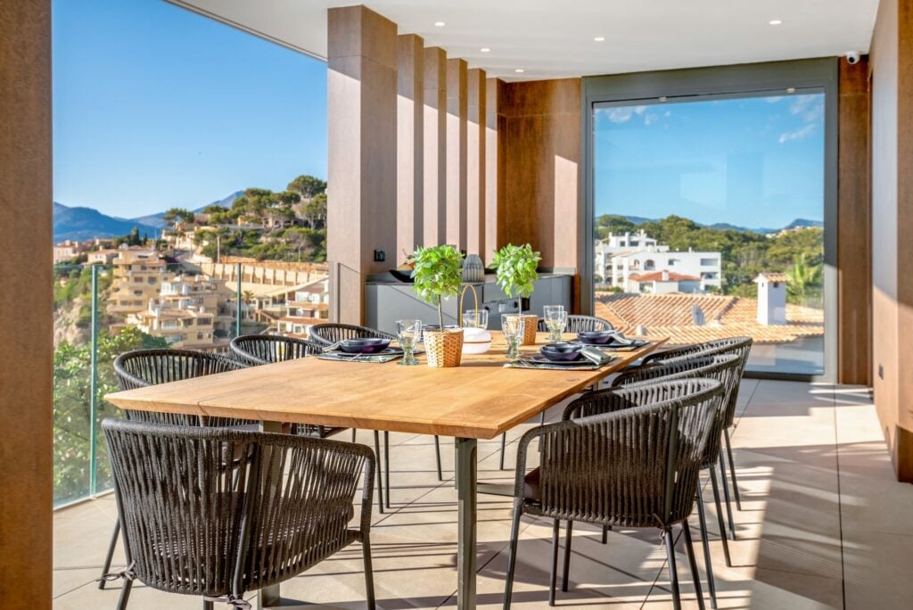 Helles, warmes Esszimmer mit großen Glaswänden, bietet Sicht auf Hügel, blauen Himmel und umliegende Häuser.