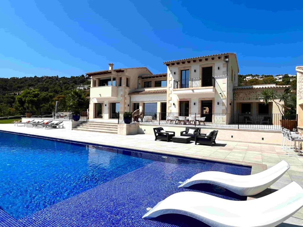 Zweistöckige Villa mit hellen Natursteinwänden, bodentiefen Fenstern, Swimmingpool mit eingelassenen Liegen und Terrassenmöbeln.