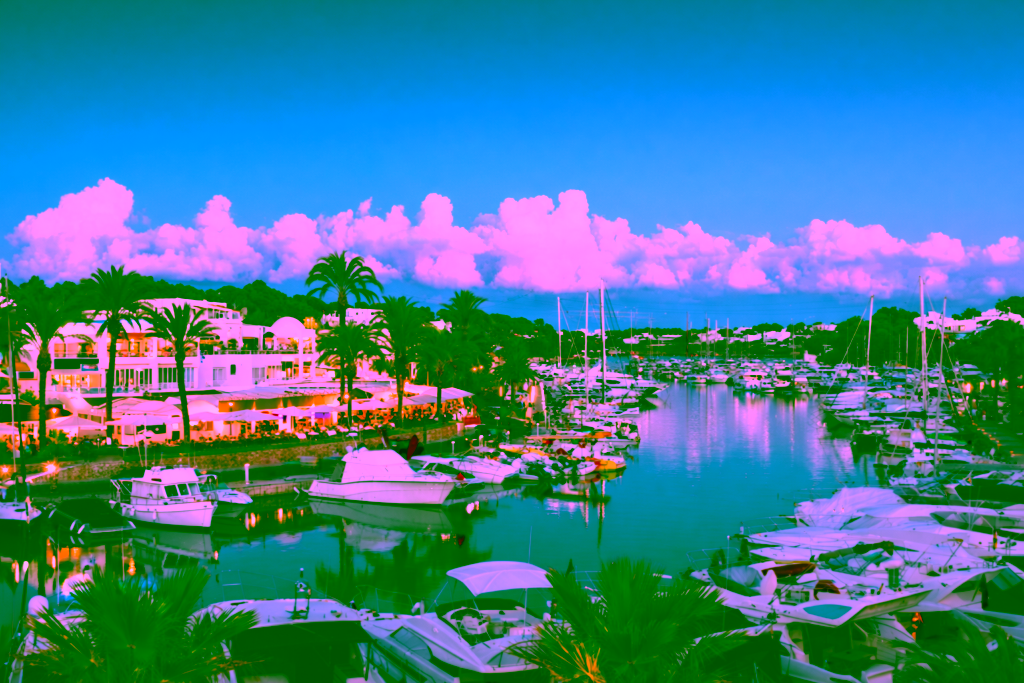 Marina with numerous boats, palm trees, and illuminated restaurants at twilight