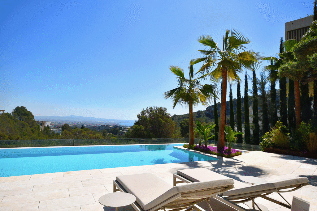 Área exterior con piscina, tumbonas y palmeras frente a vistas panorámicas de colinas y mar