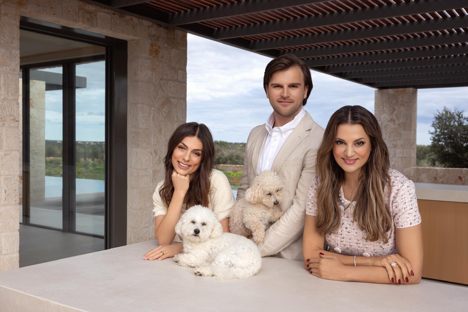 Three stylishly dressed people with two dogs on a terrace with natural stone and a wooden pergola