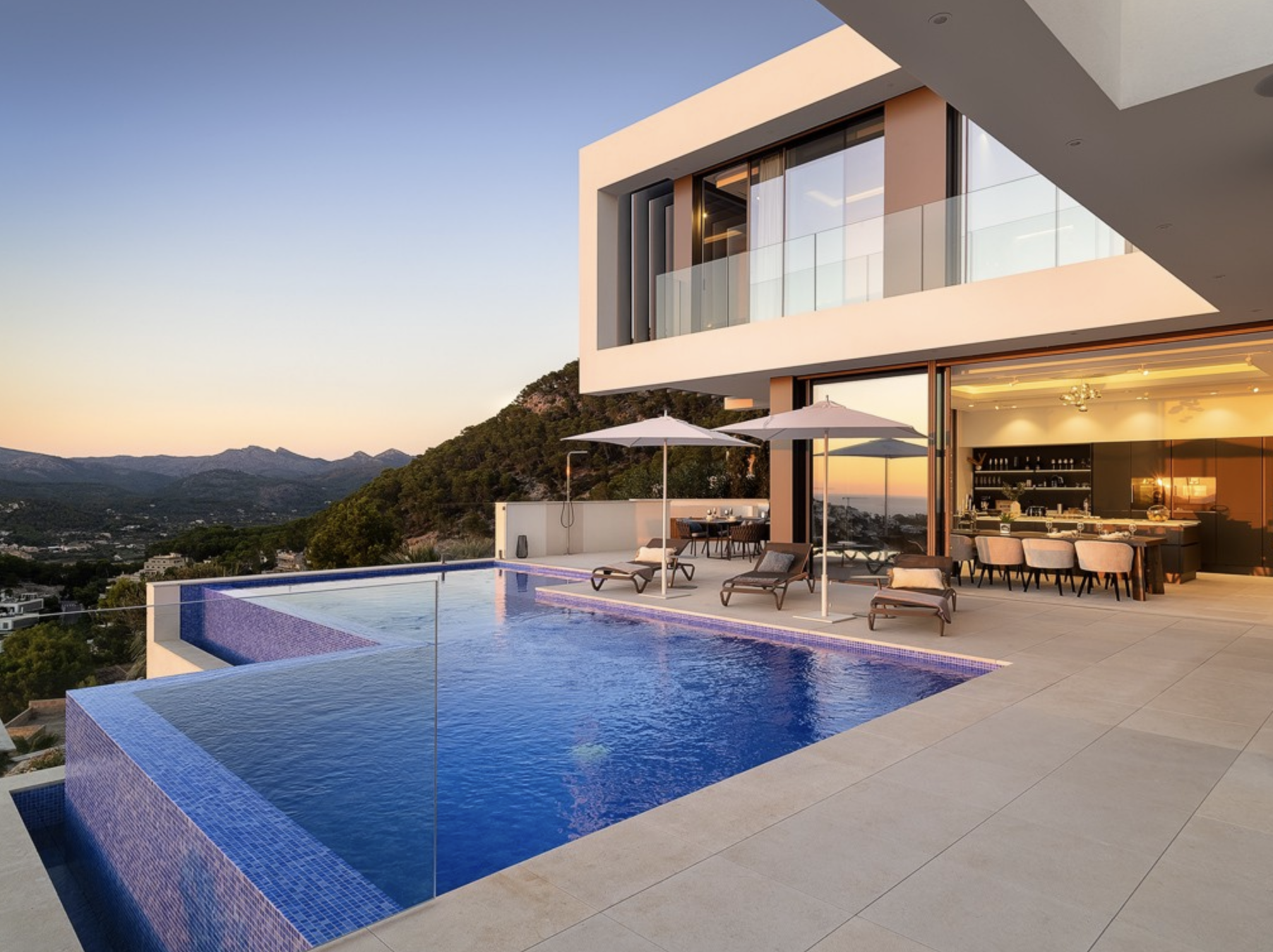 Vista exterior de una moderna villa arquitectónica de hormigón y cristal con piscina infinita.