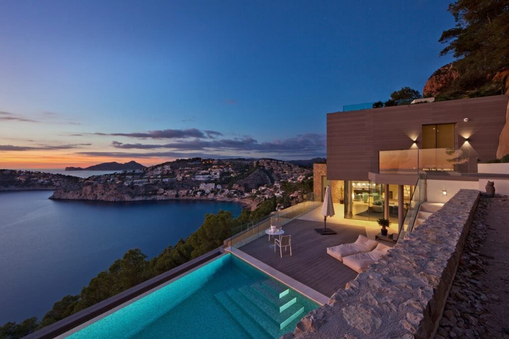 Moderne Luxusvilla mit Infinity-Pool in spektakulärer Hanglage über einer mediterranen Küstenbucht bei Sonnenuntergang