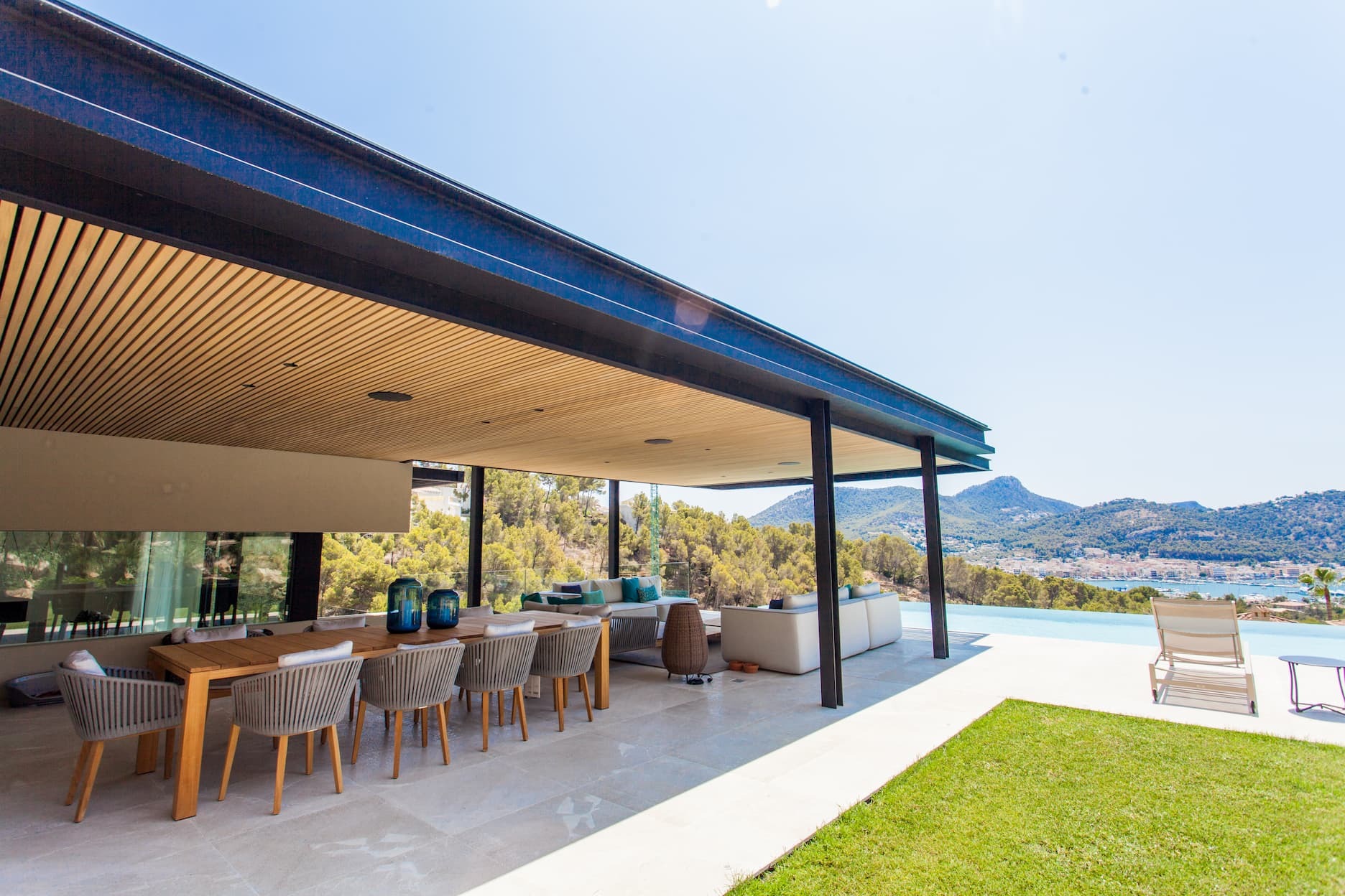 Überdachte Terrasse einer modernen Villa mit Esstisch, Lounge-Bereich und Blick auf Pool, Berge und Meer
