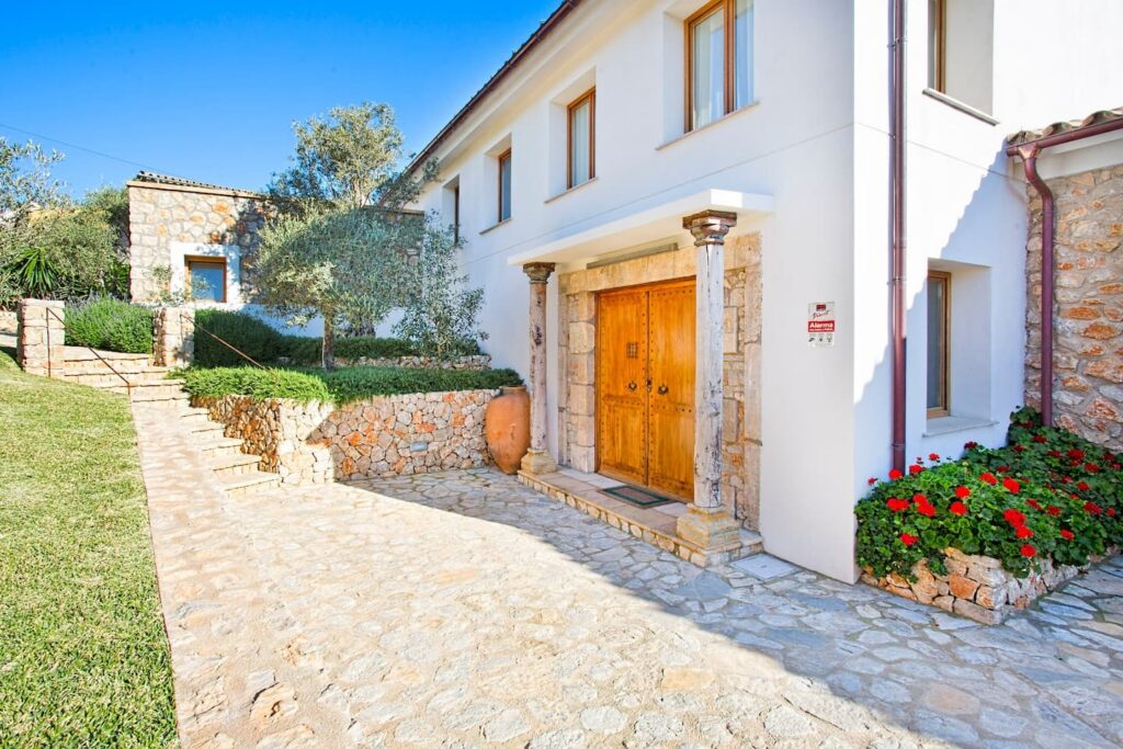 Entrada representativa con detalles en piedra natural, pórtico con columnas y puerta maciza de madera.
