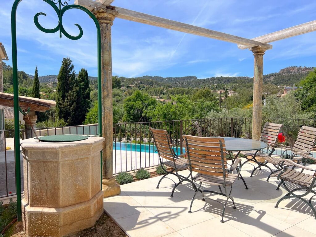 Elegante salón exterior con pérgola, piscina al fondo y vistas al paisaje montañoso.